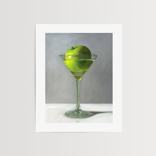 This artwork features a whimsical take on the traditional Apple Martini cocktail. A single granny smith apple rests inside a martini glass on a light, reflective surface with dramatic light and shadows.