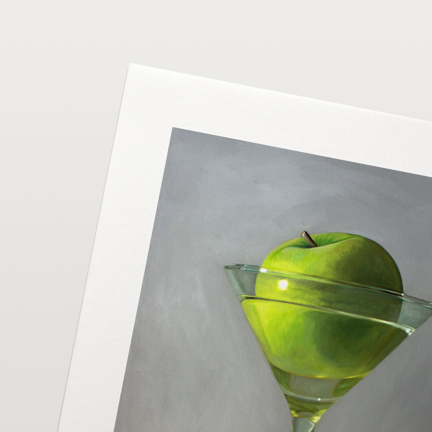 This artwork features a whimsical take on the traditional Apple Martini cocktail. A single granny smith apple rests inside a martini glass on a light, reflective surface with dramatic light and shadows.