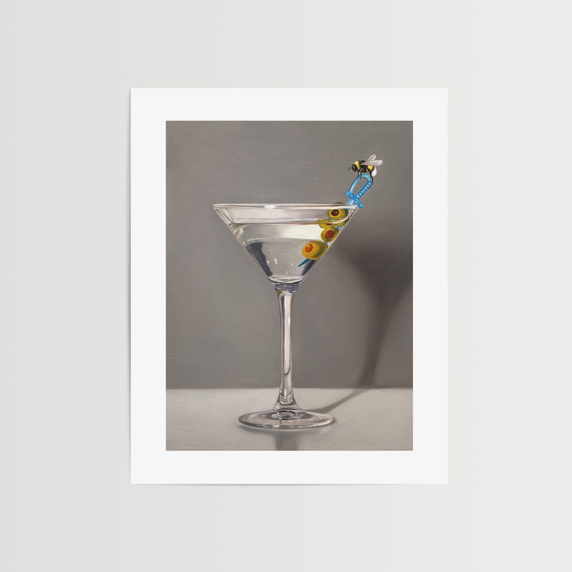 This artwork features a martini with a bumble bee perched on a blue plastic cocktail sword with a trio of green olives and a neutral, minimalistic backdrop.