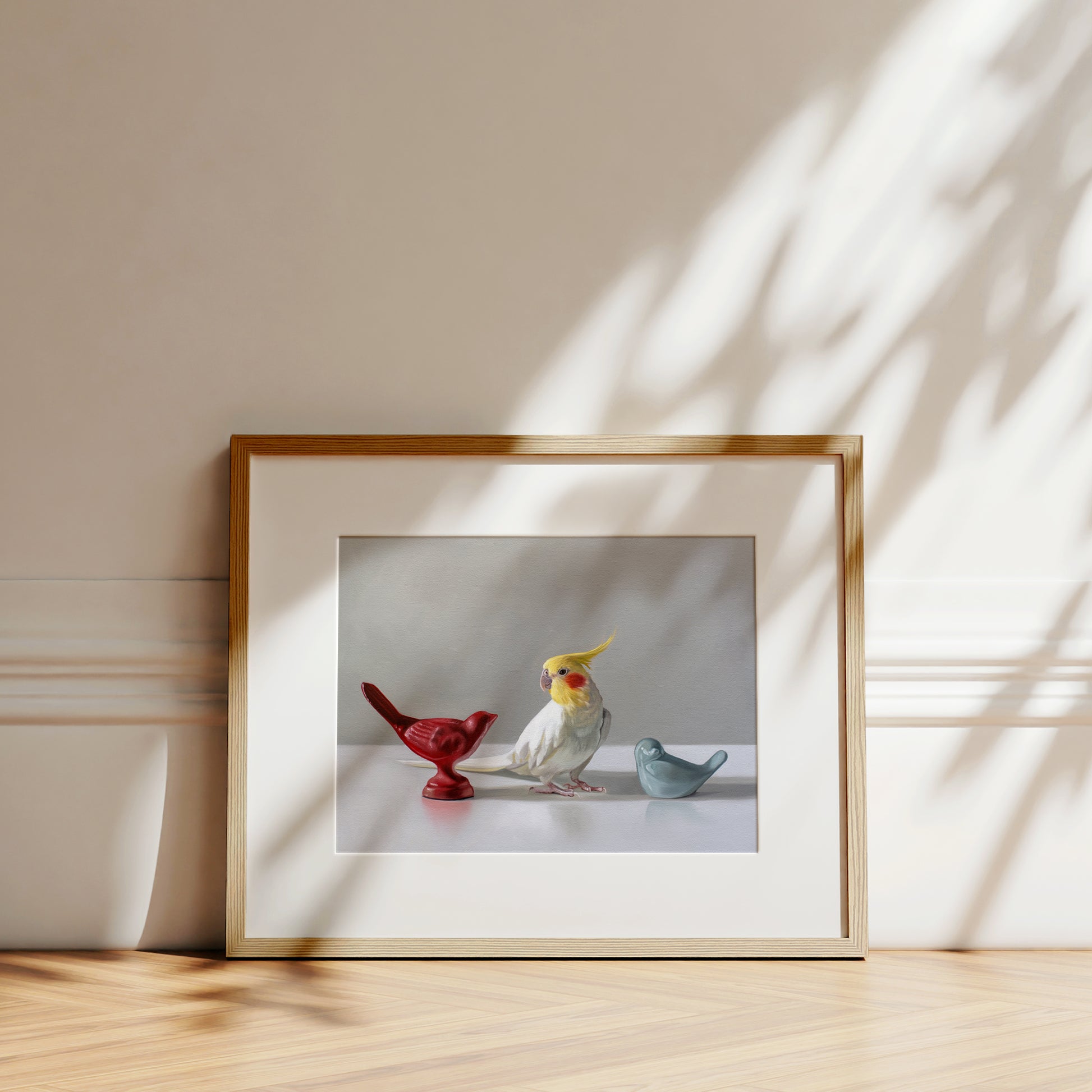 This artwork features a white cockatiel standing in between a red and blue bird figurine on a light, reflective surface with dramatic lighting.