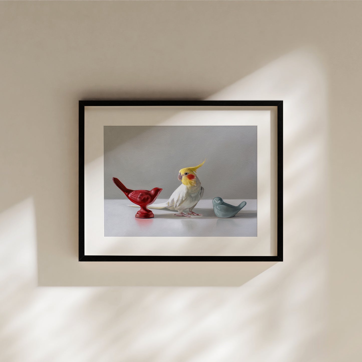 This artwork features a white cockatiel standing in between a red and blue bird figurine on a light, reflective surface with dramatic lighting.