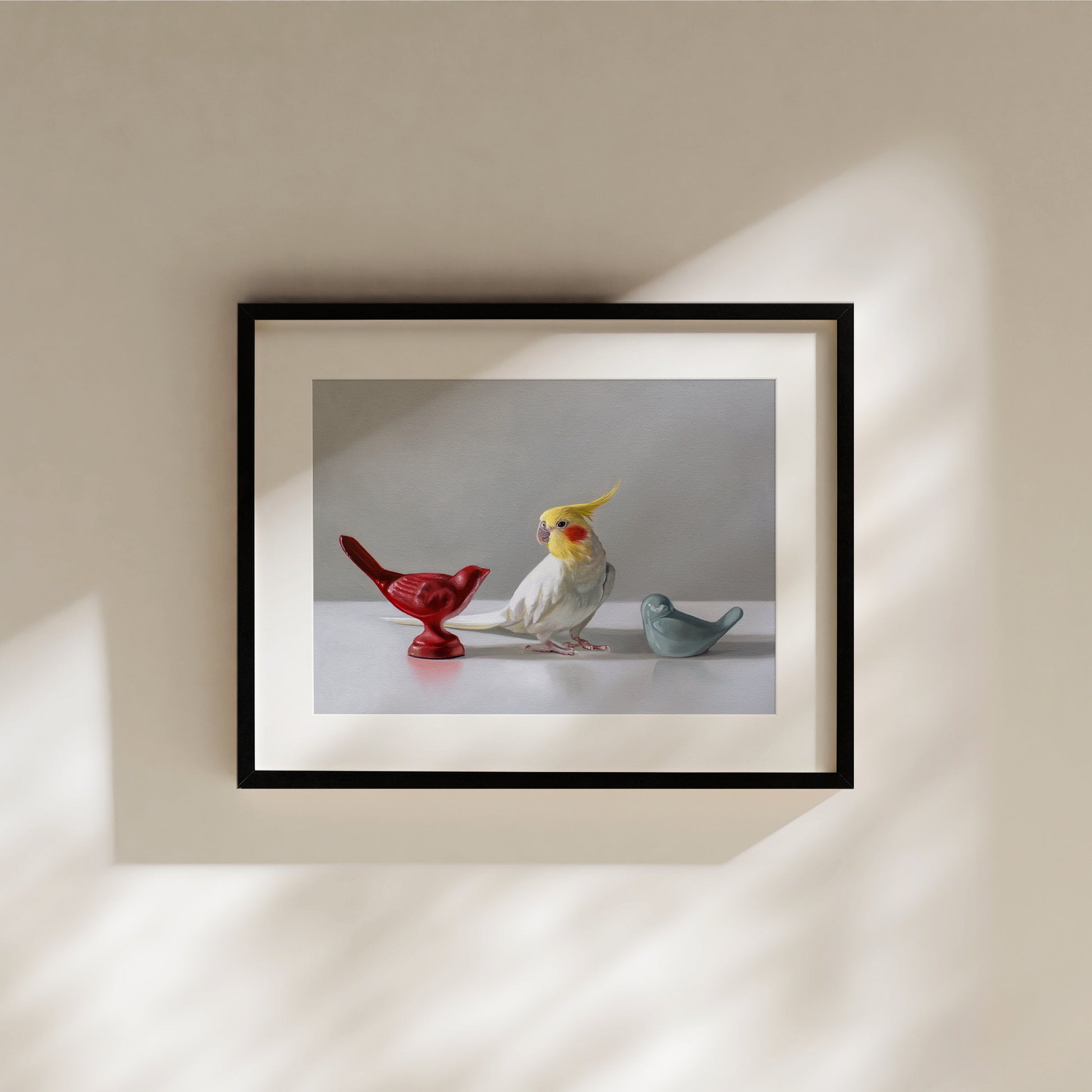 This artwork features a white cockatiel standing in between a red and blue bird figurine on a light, reflective surface with dramatic lighting.