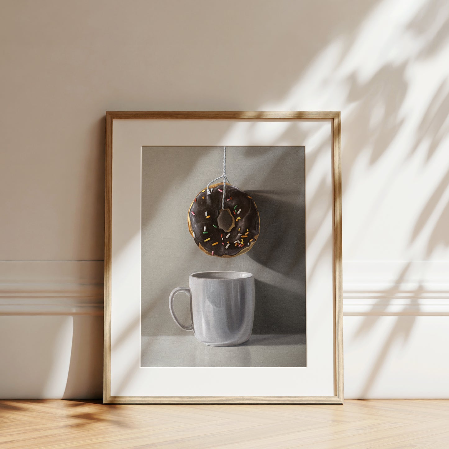 This artwork features a chocolate sprinkled doughnut suspended by a string over a white porcelain cup.