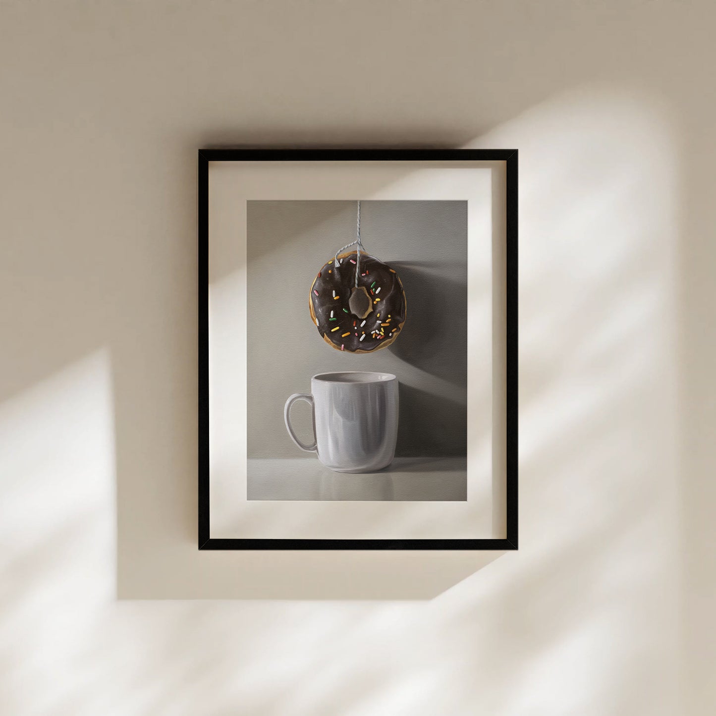 This artwork features a chocolate sprinkled doughnut suspended by a string over a white porcelain cup.