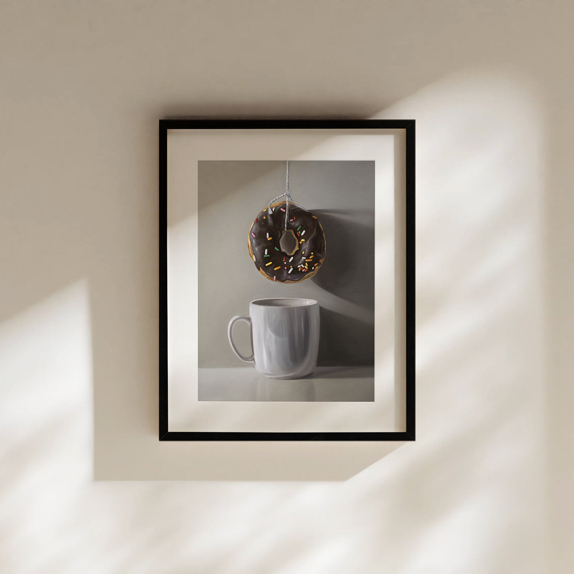 This artwork features a chocolate sprinkled doughnut suspended by a string over a white porcelain cup.