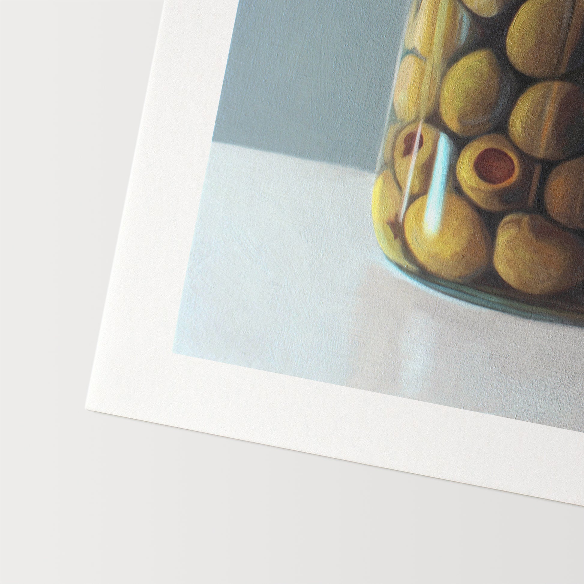 This artwork features a jar of green olives resting on a light, reflective surface with a muted blue/green background.