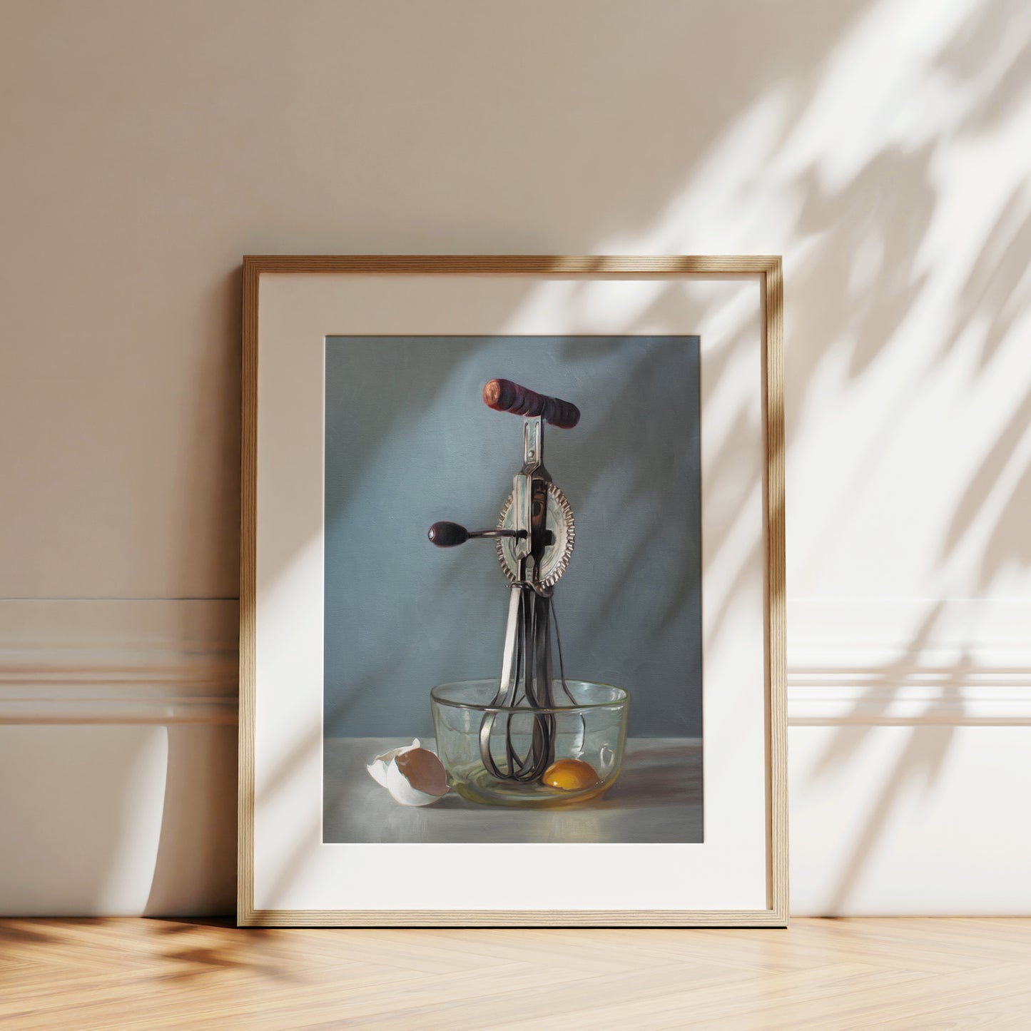 This artwork features an antique egg beater and a glass bowl containing an egg white the white shells juxtaposed on the left.