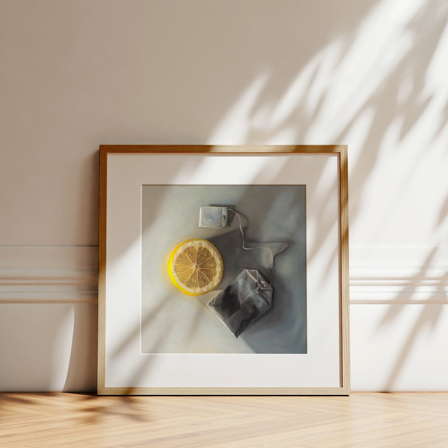 This artwork features a slice of lemon laying next to a tea bag on a light grey surface with dramatic lighting and cast shadows.