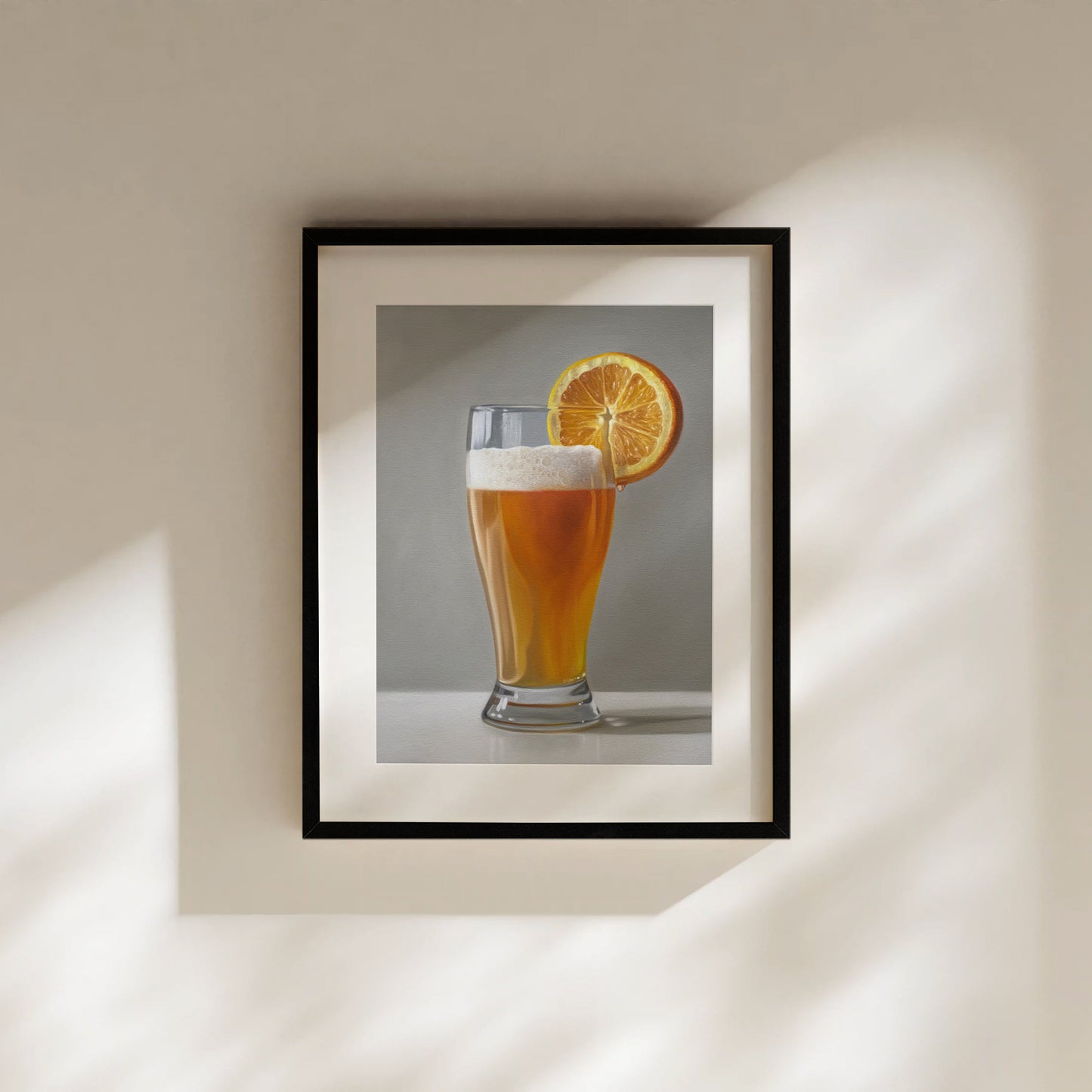 Framed fine art print of a golden beer shandy with a bright orange slice, on a light wall.