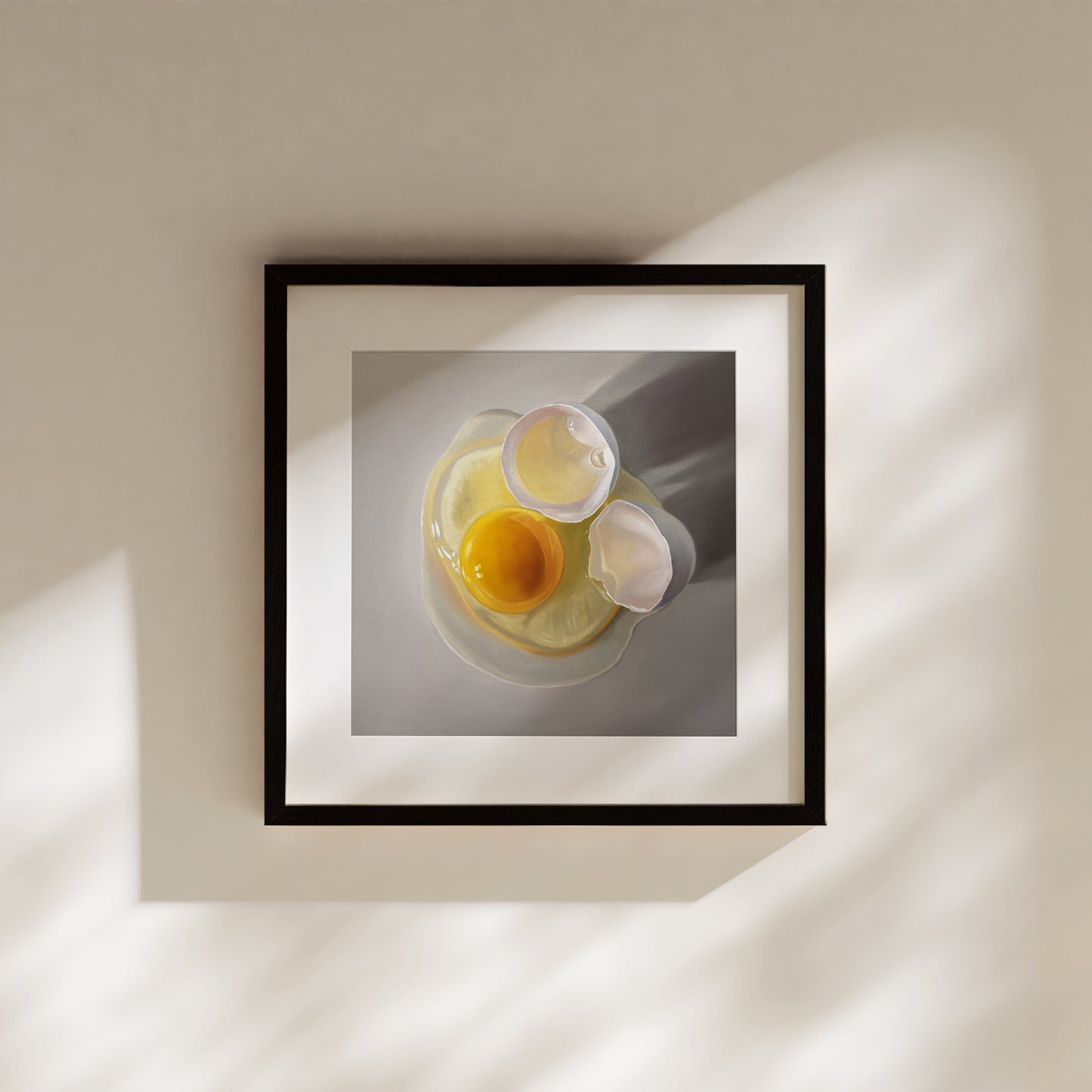 Framed fine art print of a cracked egg with a vibrant yellow yolk and white shell on a gray background.