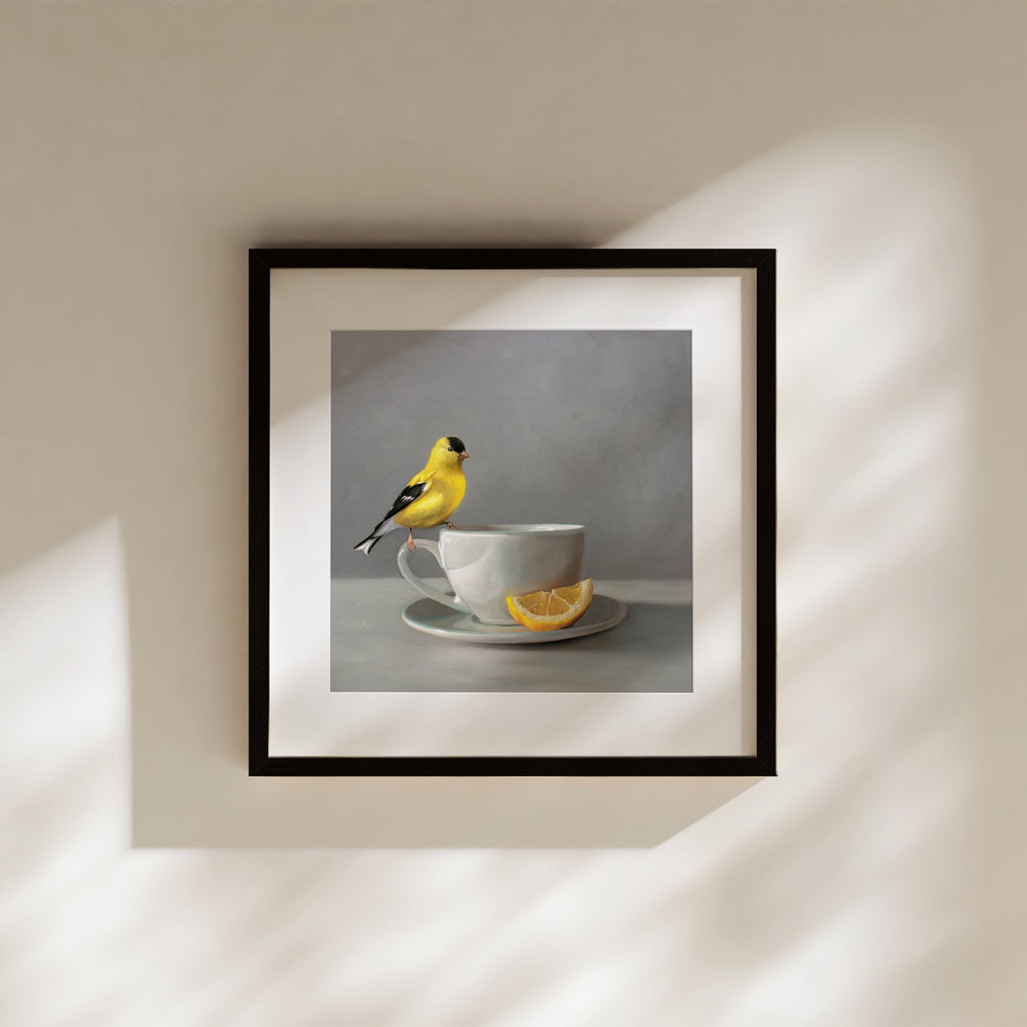 Framed fine art print of a yellow goldfinch perched on a grey teacup with a lemon slice.
