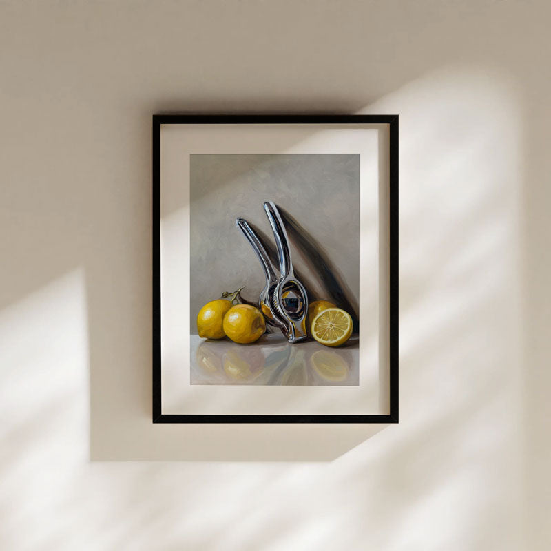 Fine art print of a metallic citrus press and yellow lemons in a black frame with a white mat border.