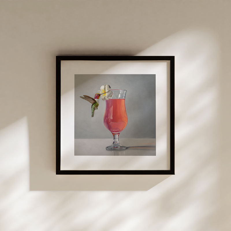 Framed fine art print of a hummingbird hovering by a pink cocktail garnished with a white flower.