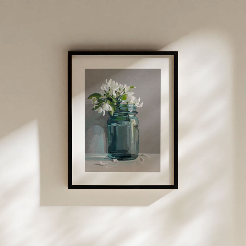 Fine art print of white apple blossoms in a teal glass jar, framed in black on a neutral wall with soft light.