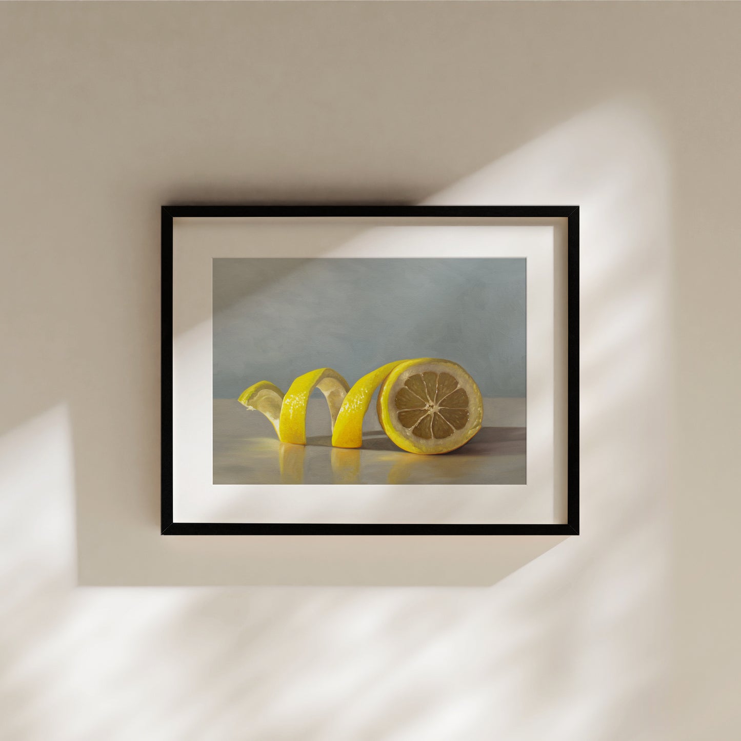 Black-framed fine art print of a vibrant yellow lemon peel twisting around a halved lemon on a light surface.