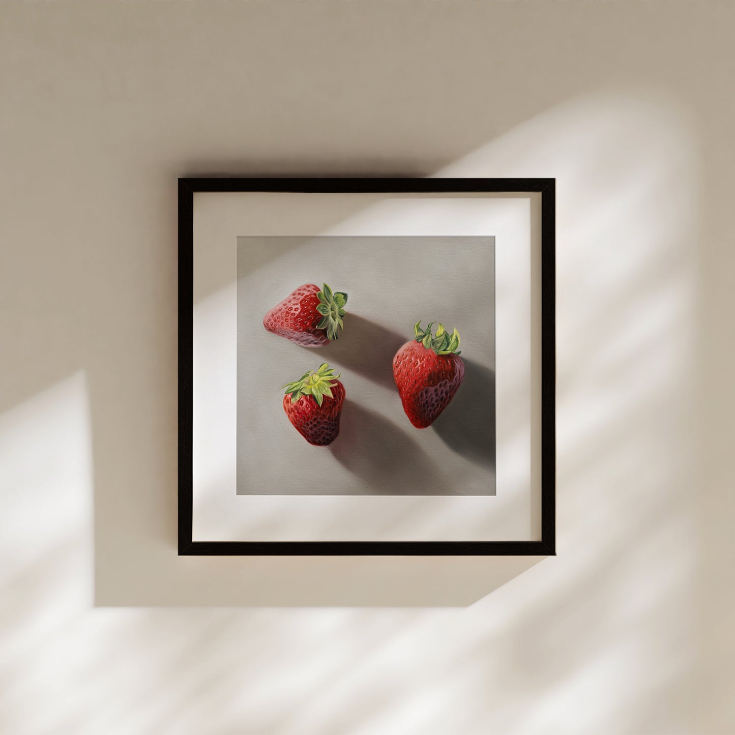 Framed fine art print of three vibrant red strawberries with green stems on a light gray background.