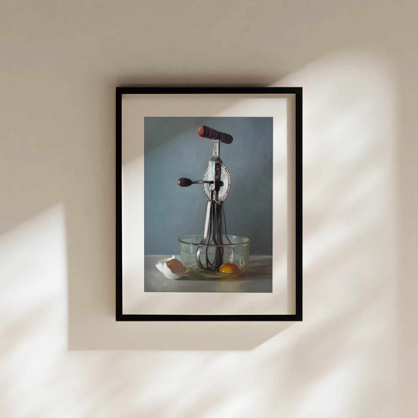 Framed fine art print of a vintage egg beater, glass bowl with yolk, and eggshell.