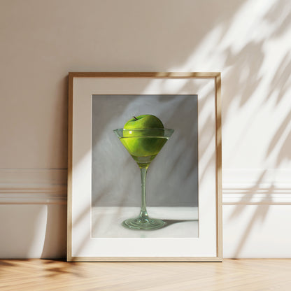 This artwork features a whimsical take on the traditional Apple Martini cocktail. A single granny smith apple rests inside a martini glass on a light, reflective surface with dramatic light and shadows.