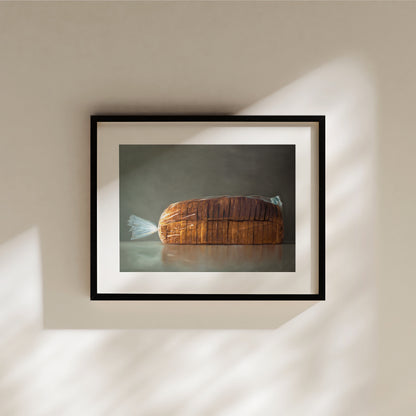 This artwork features a fresh loaf of bread in clear plastic wrap on a medium grey background.