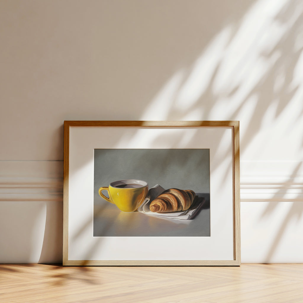 This artwork features a yellow cup of coffee and fresh croissant on a napkin.