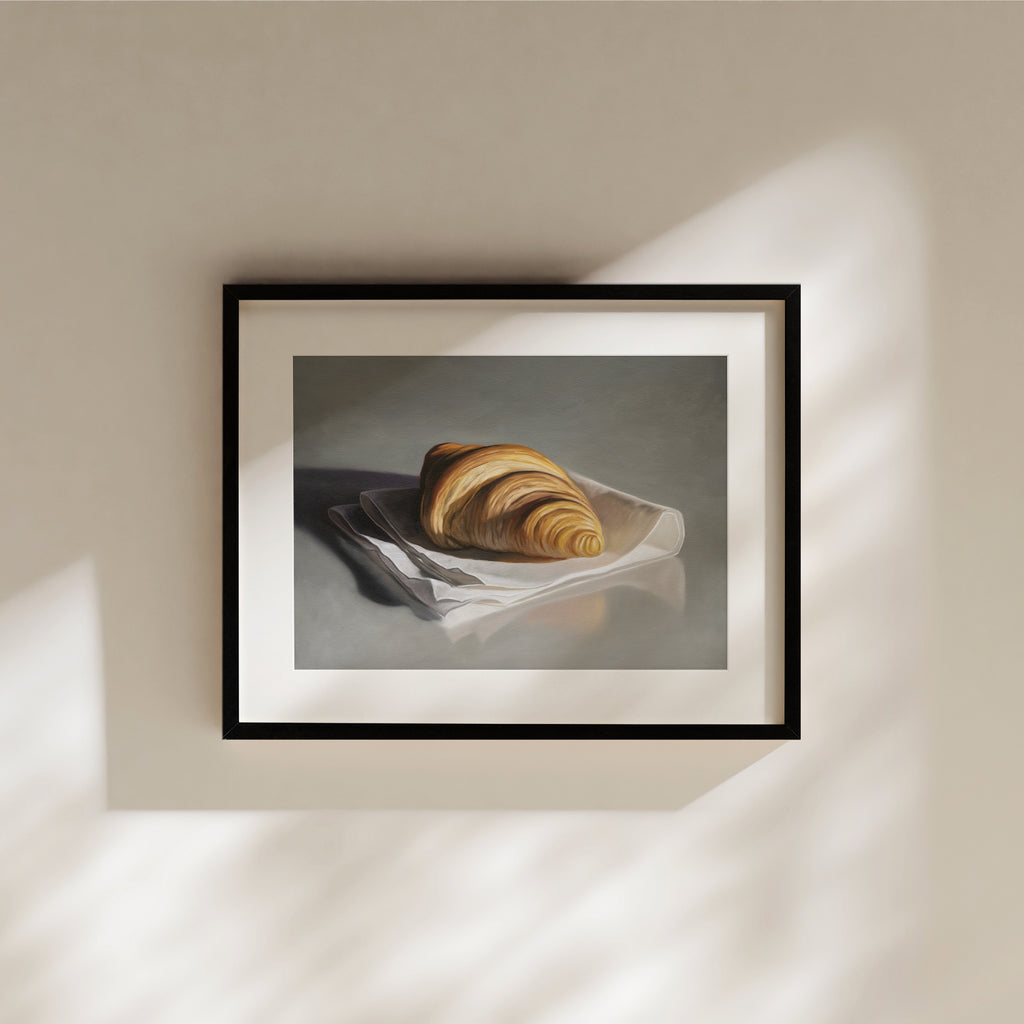 This artwork features a single freshly baked croissant resting on a napkin on a reflective surface.