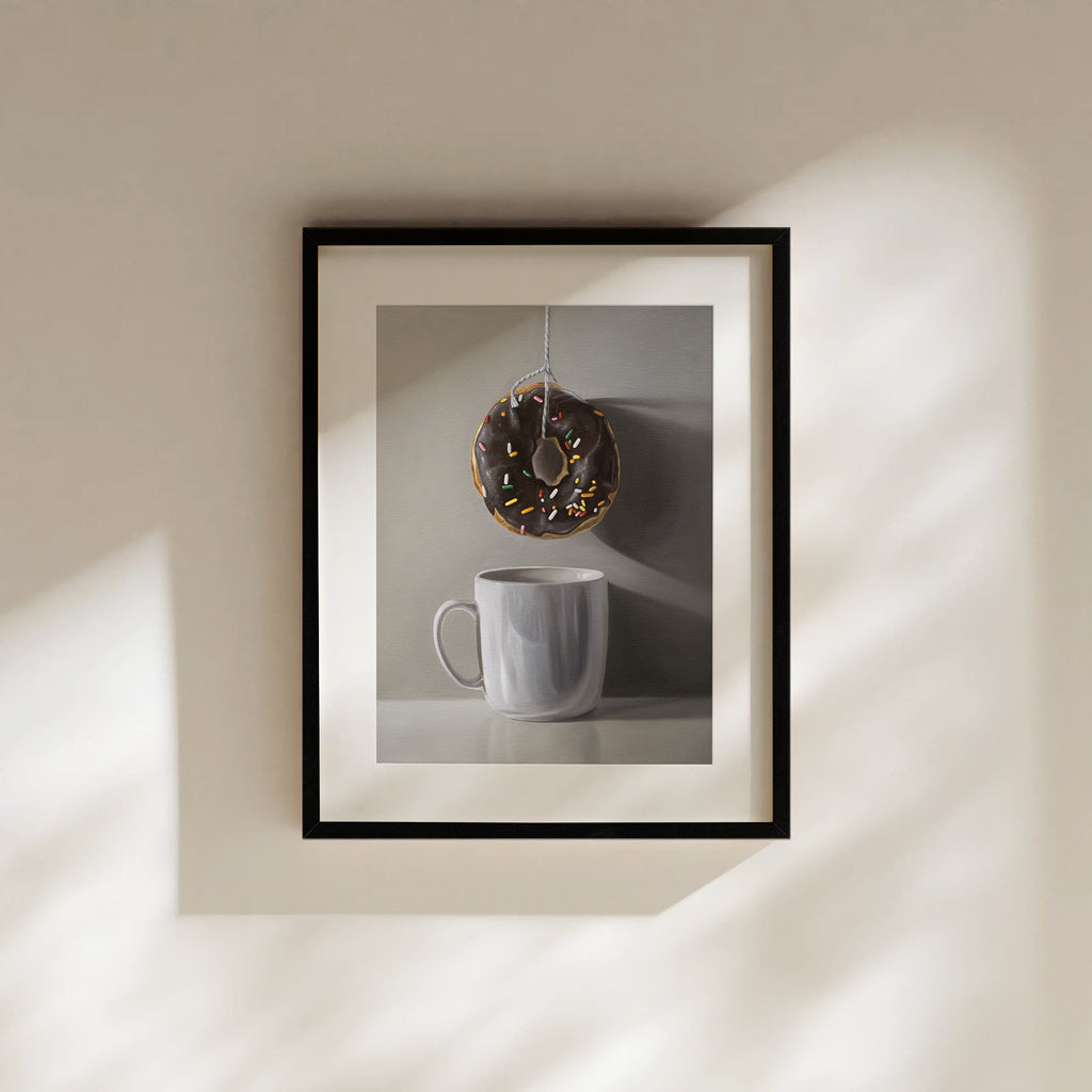 This artwork features a chocolate sprinkled doughnut suspended by a string over a white porcelain cup.