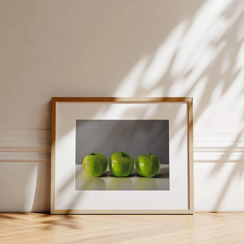 This artwork features a trio of bright green granny smith apples resting on a light, reflective surface with a neutral grey background.
