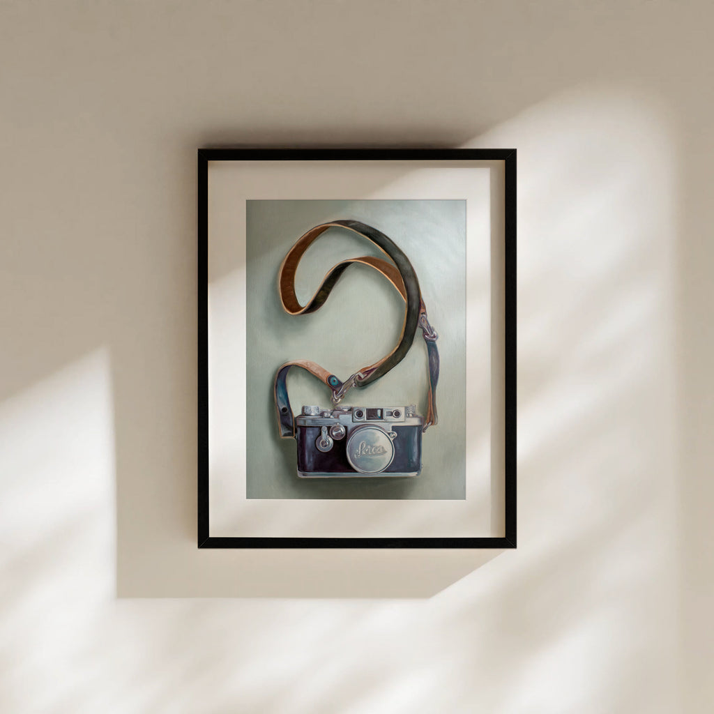 This artwork features a vintage Leica camera with a leather strap strategically layed out on a light surface.