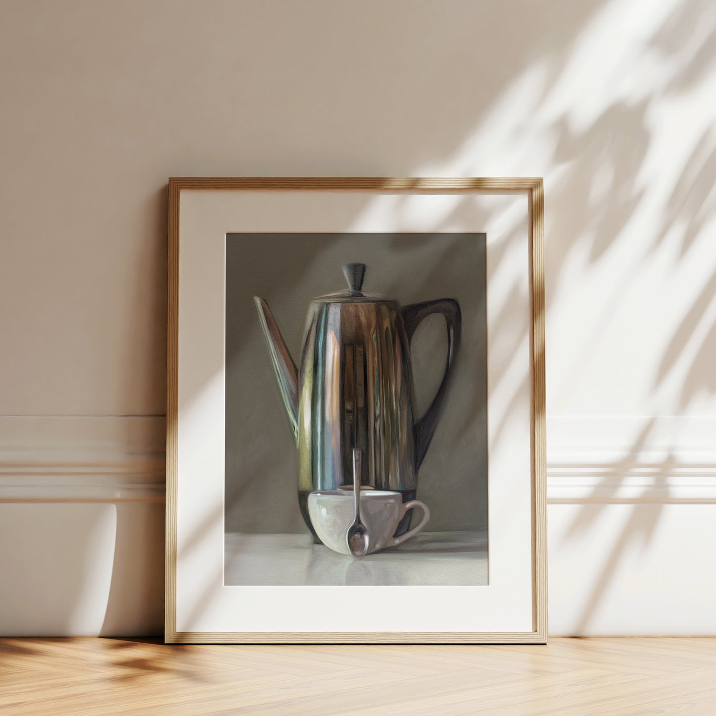 This artwork features a reflective percolator, porcelain coffee cup and small spoon resting on a light reflective surface with neutral grey tones.