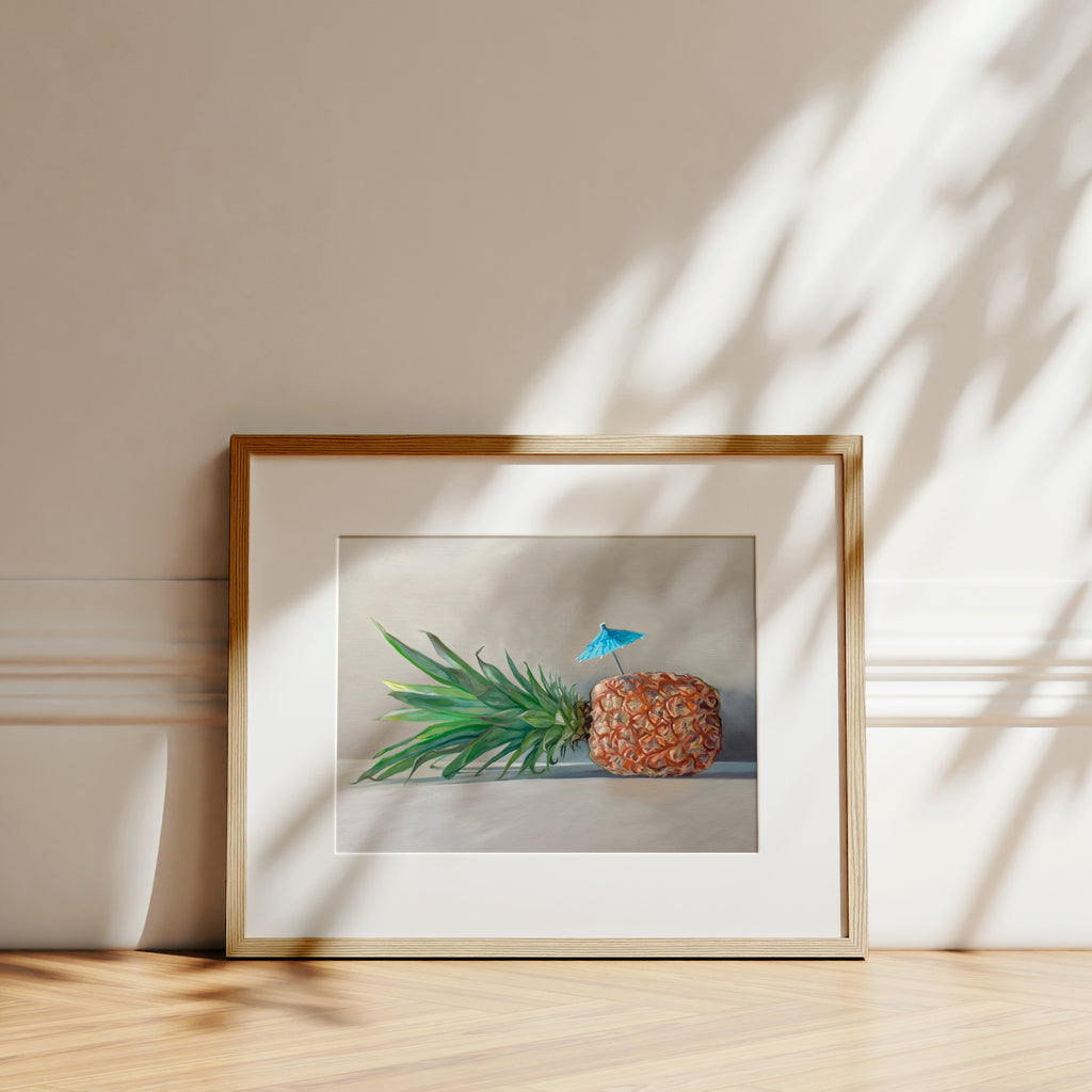 This artwork features a sideways resting pineapple with a blue tropical drink umbrella on top.