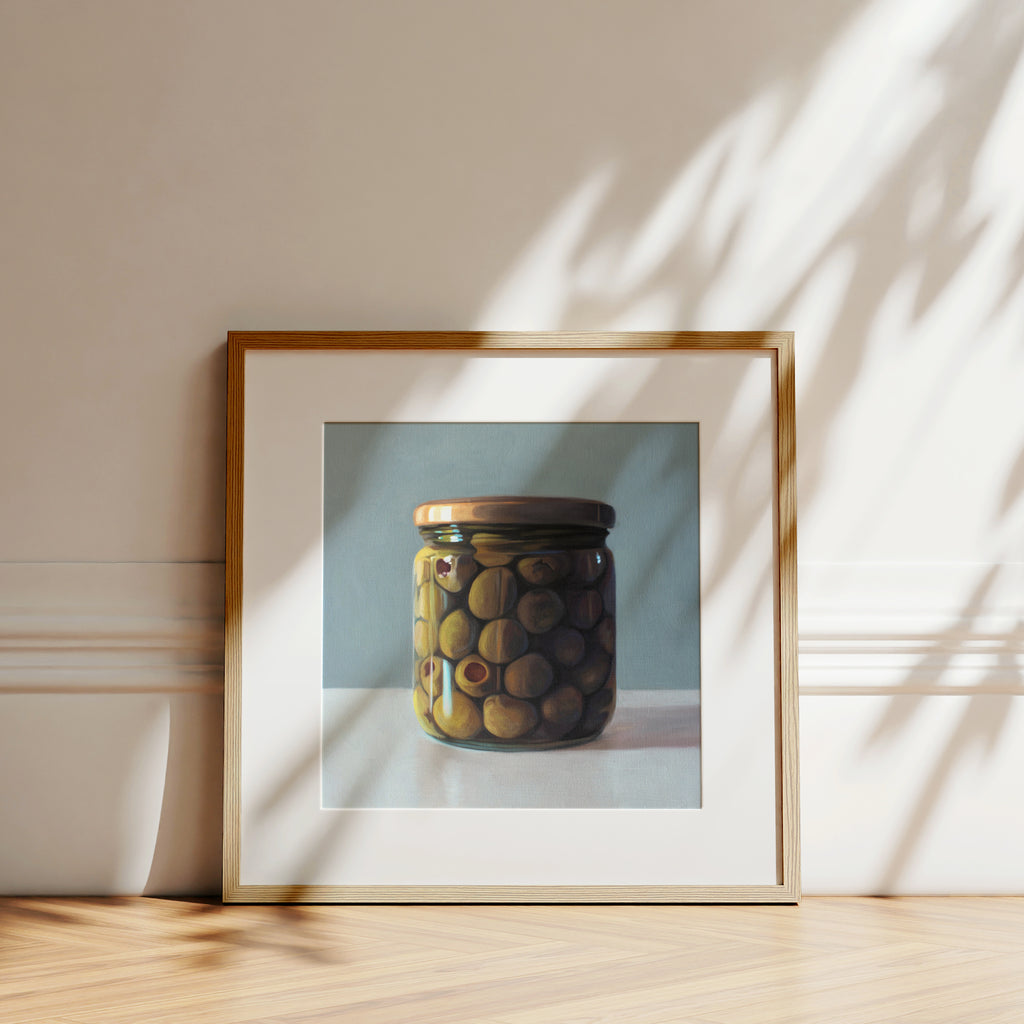 This artwork features a jar of green olives resting on a light, reflective surface with a muted blue/green background.