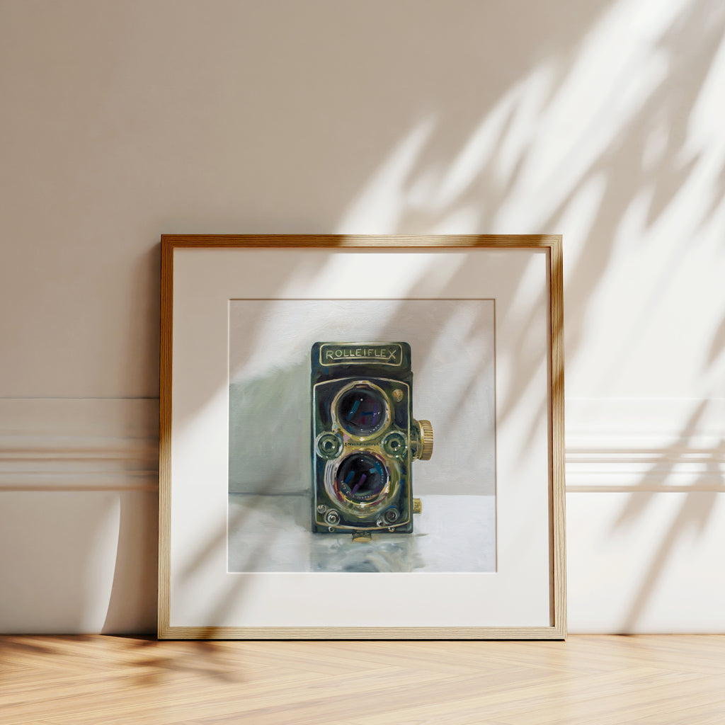This artwork features a vintage film camera on a light reflective surface and grey background.