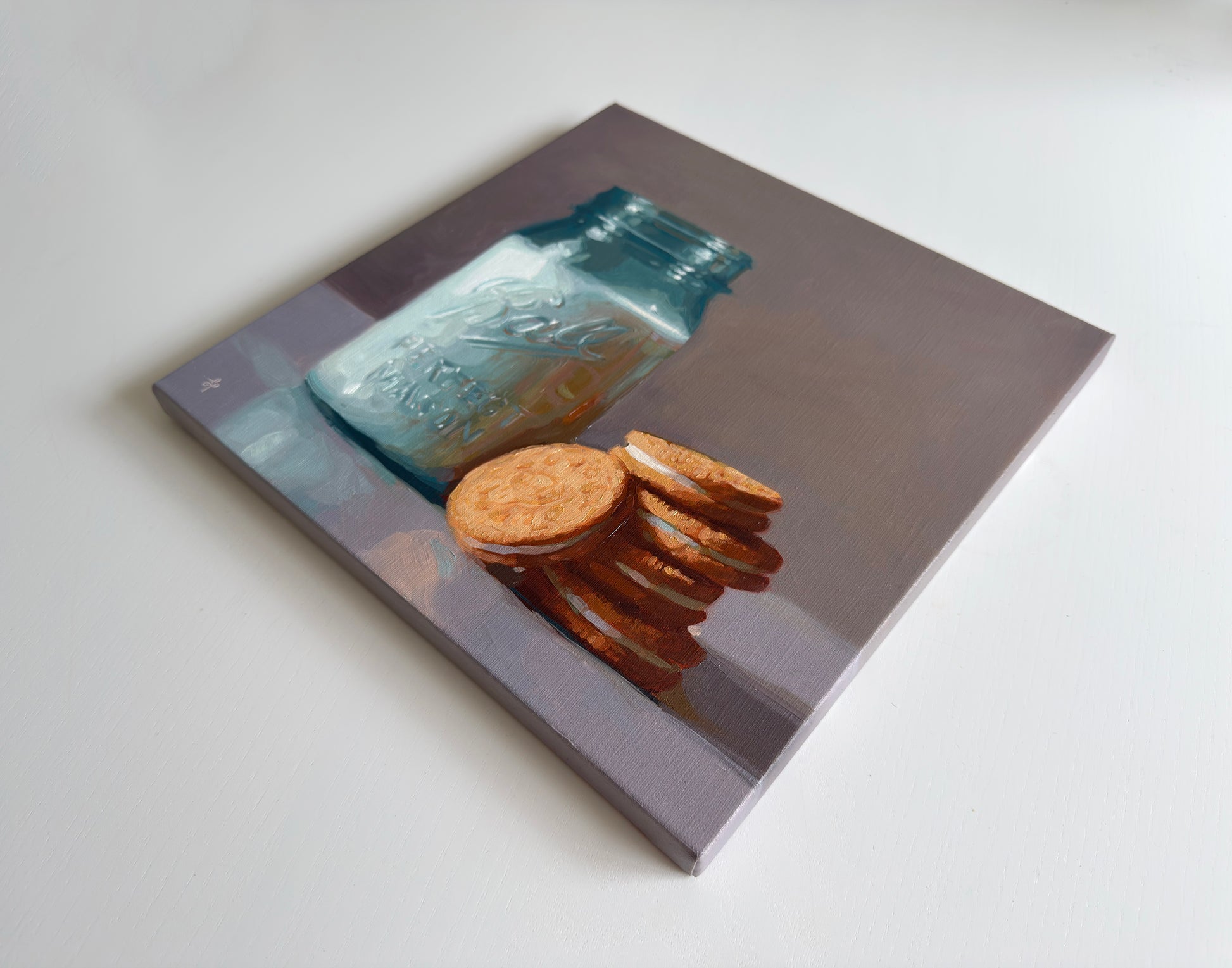 A square canvas painting depicting a blue glass mason jar and a stack of golden-brown cookies, shown at an angle on a light gray background.
