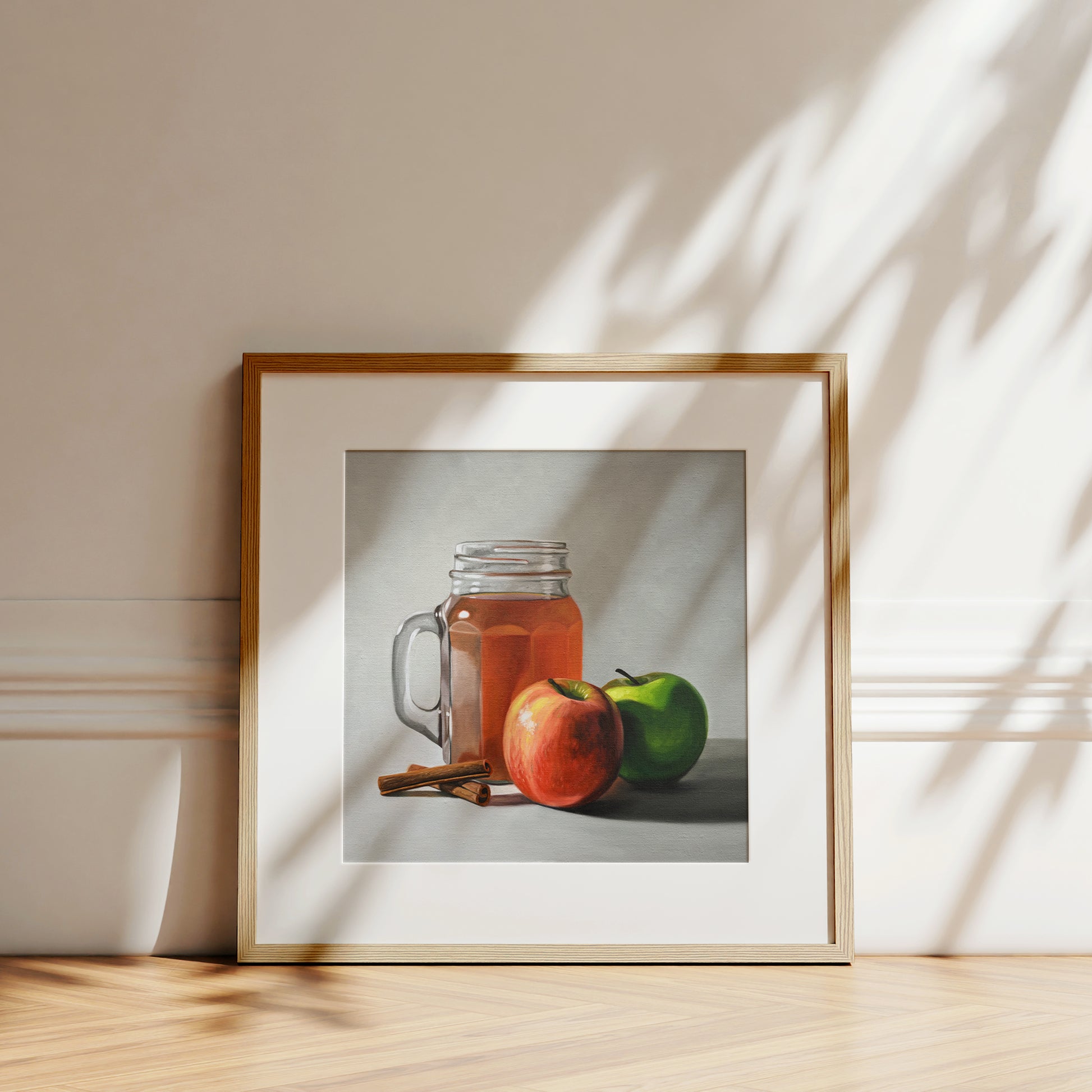 Fine art print of a mason jar of apple cider, red and green apples, and cinnamon sticks in a light wood frame.