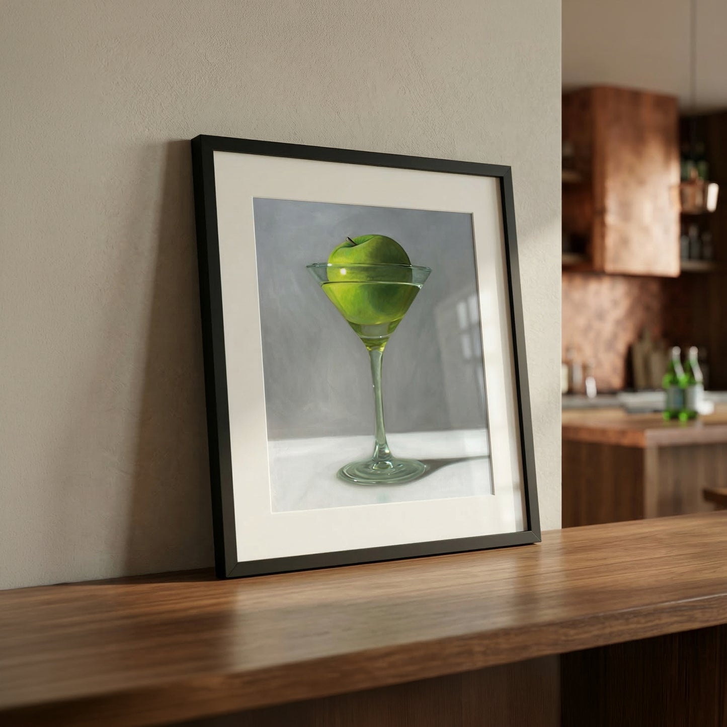 Framed fine art print of a vibrant green apple in a martini glass, displayed on a wooden counter.