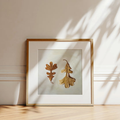 Autumn Oak Tree Leaves Fine Art Print by Lauren Pretorius: a duo of Oak Tree leaves laying on a light surface. One of the leaves faces upwards, while the other is flipped over and upside down.