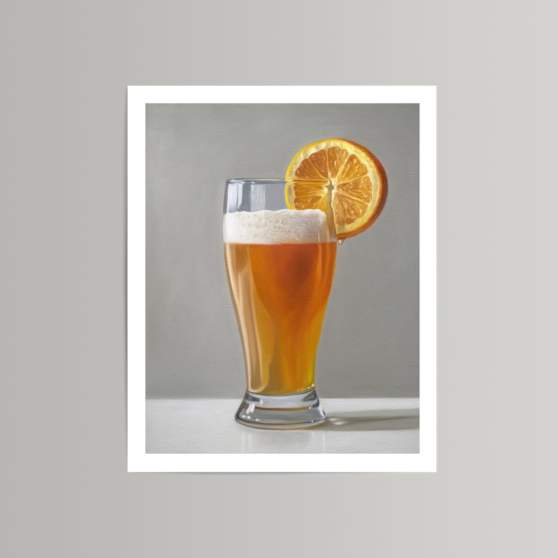 Fine art print of a golden beer shandy with a frothy head and an orange slice on a light gray background.