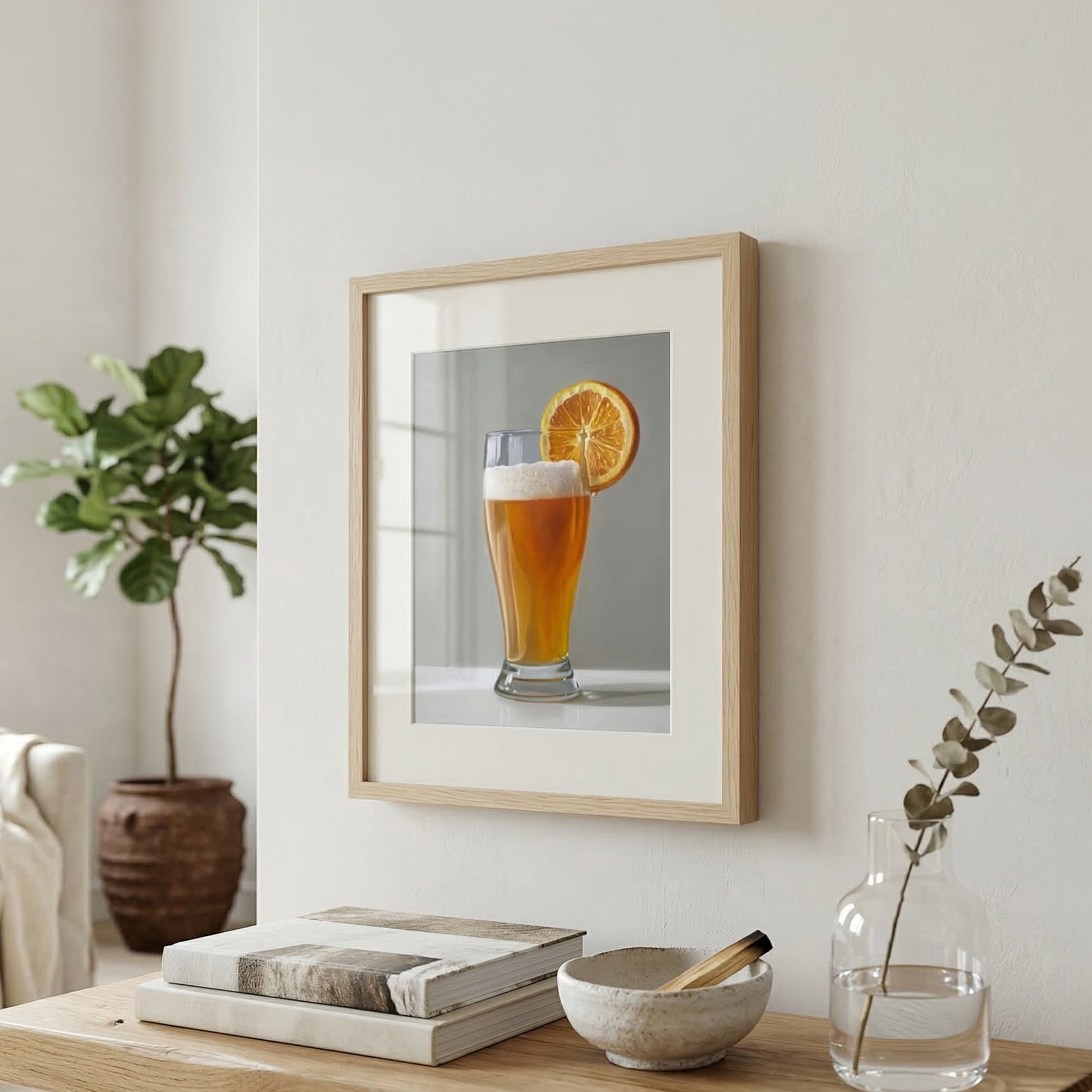 Fine art print of a beer shandy with an orange slice in a light wood frame, hanging on a white wall.