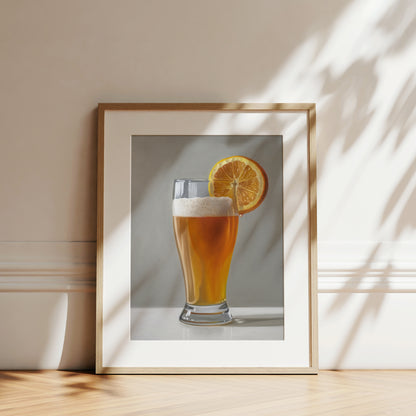 Framed fine art print of a golden beer shandy with an orange slice, on a light background.