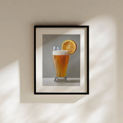 Framed fine art print of a golden beer shandy with a bright orange slice, on a light wall.