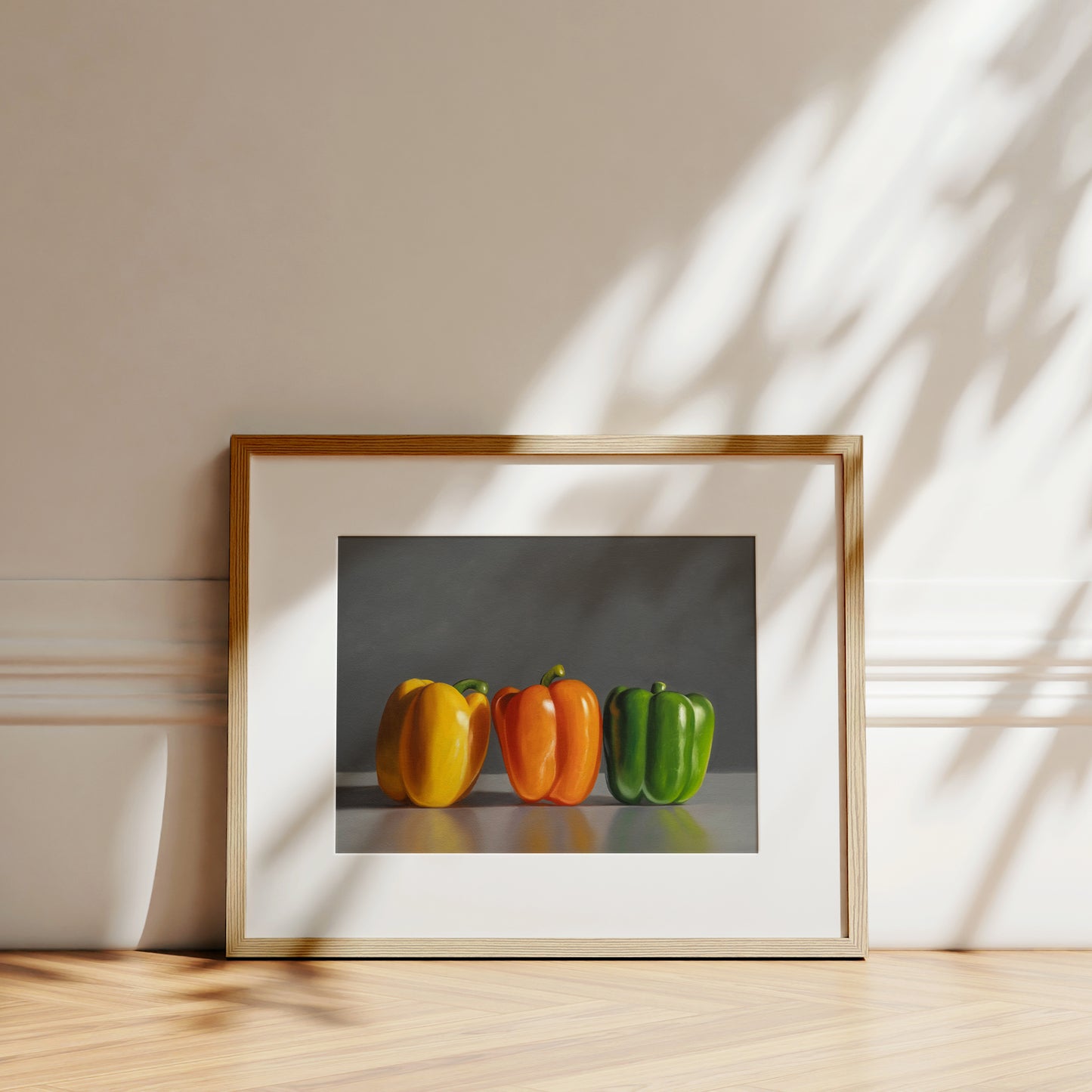 Framed fine art print of three vibrant bell peppers: yellow, orange, and green, on a light wood floor.