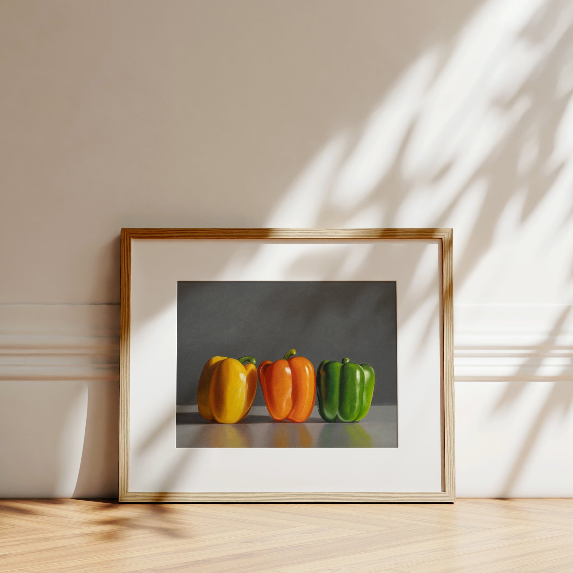 Framed fine art print of three vibrant bell peppers: yellow, orange, and green, on a light wood floor.