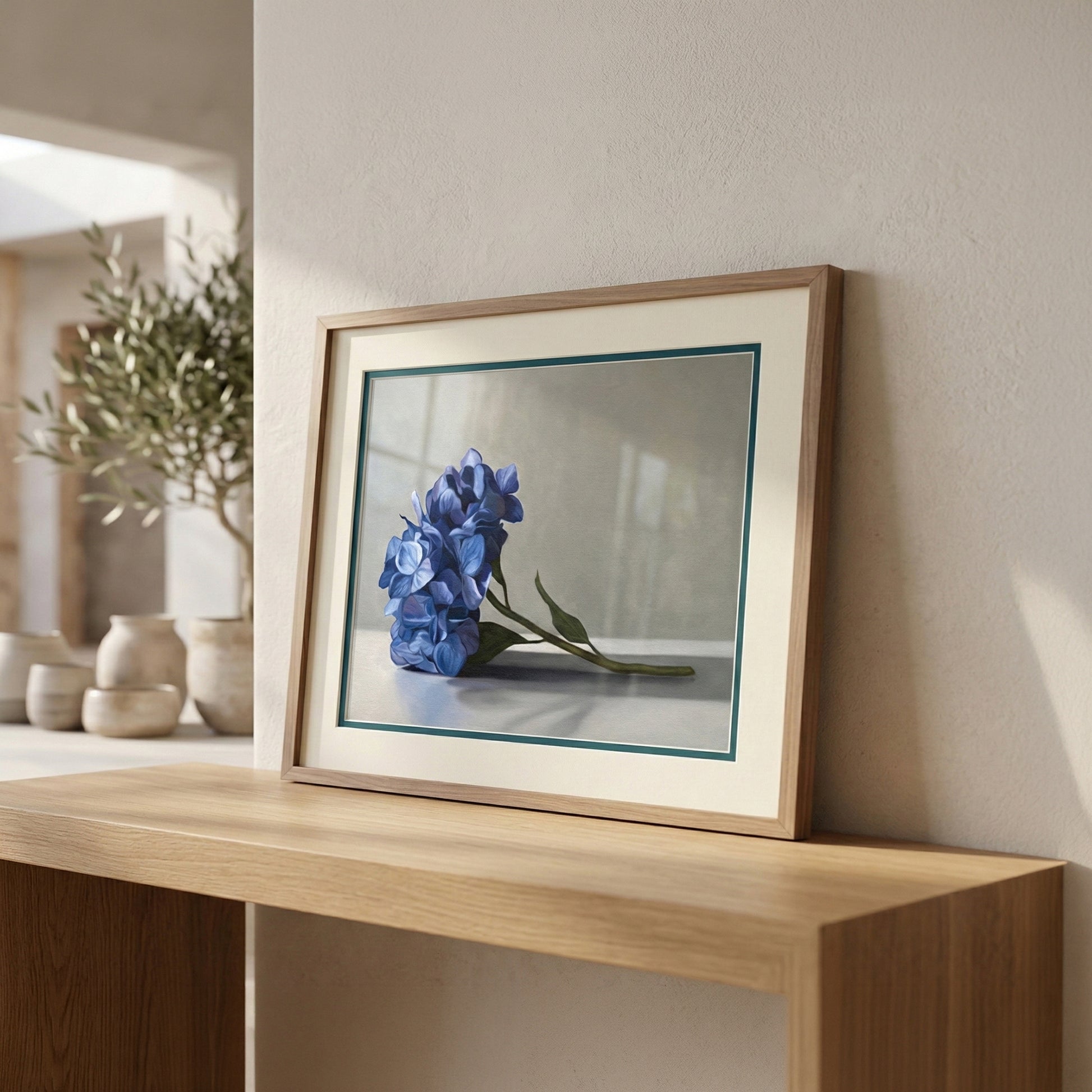 Framed blue hydrangea fine art print with a white mat and thin green border on a wooden shelf.