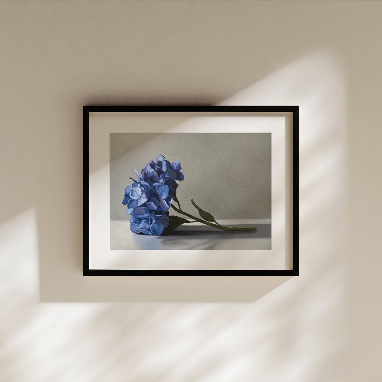 Framed fine art print of vibrant blue hydrangeas on a light background, hanging on a cream wall.