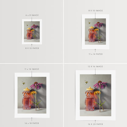 Bumble Bee, Honey & Blossoms Fine Art Print by Lauren Pretorius: a bottle of honey shaped as a bear and a pair of flowers with a bumble bee flying in to inspect.