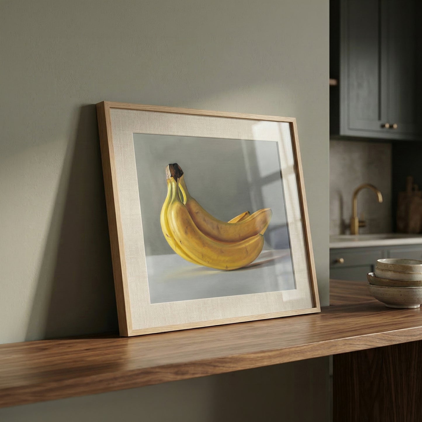 Still life fine art print of a bunch of yellow bananas in a light wood frame, leaning on a wooden shelf.
