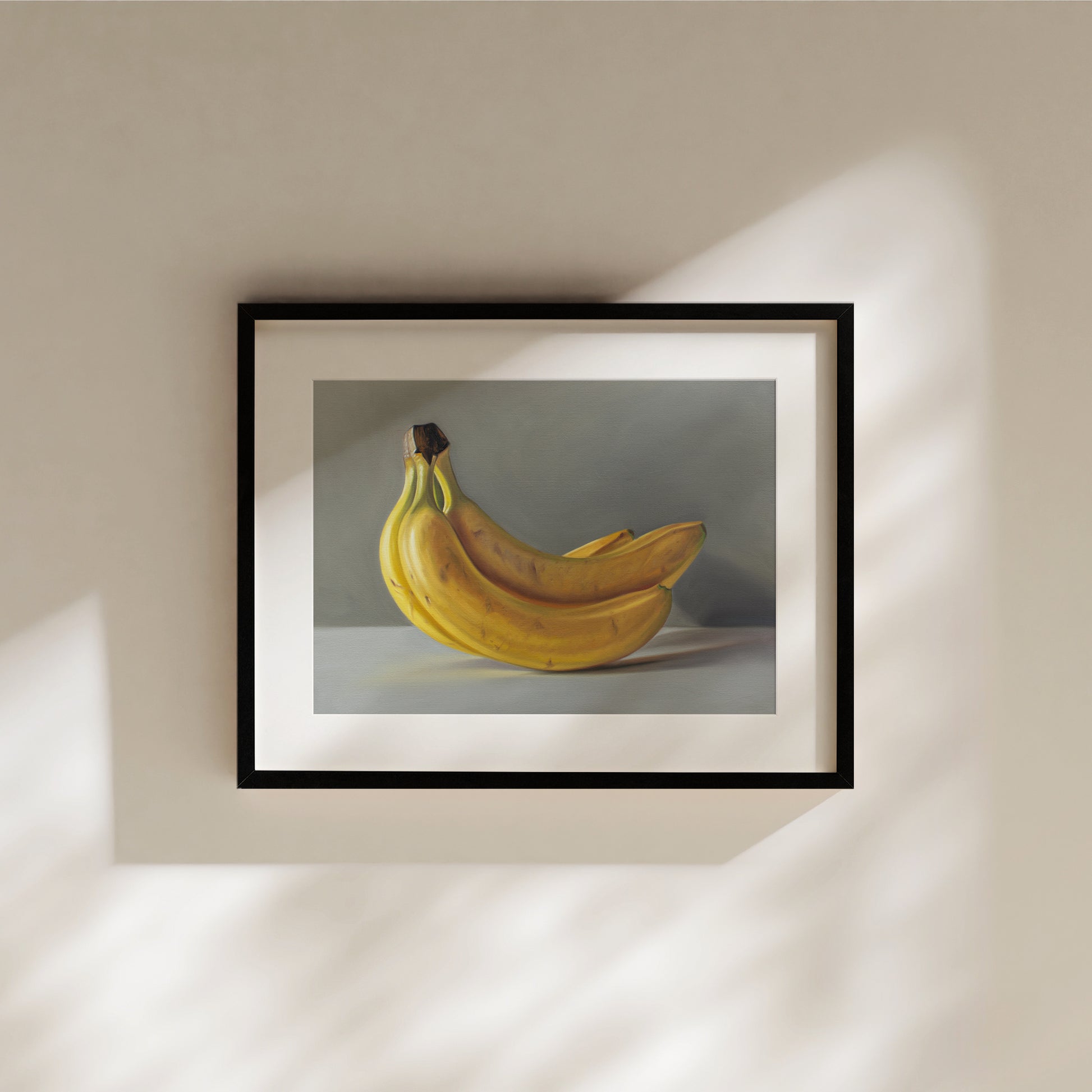 Framed fine art print of a vibrant yellow bunch of bananas against a gray background, hanging on a beige wall.
