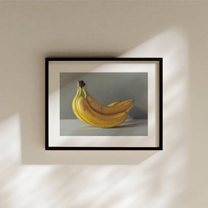 Framed fine art print of a vibrant yellow bunch of bananas against a gray background, hanging on a beige wall.