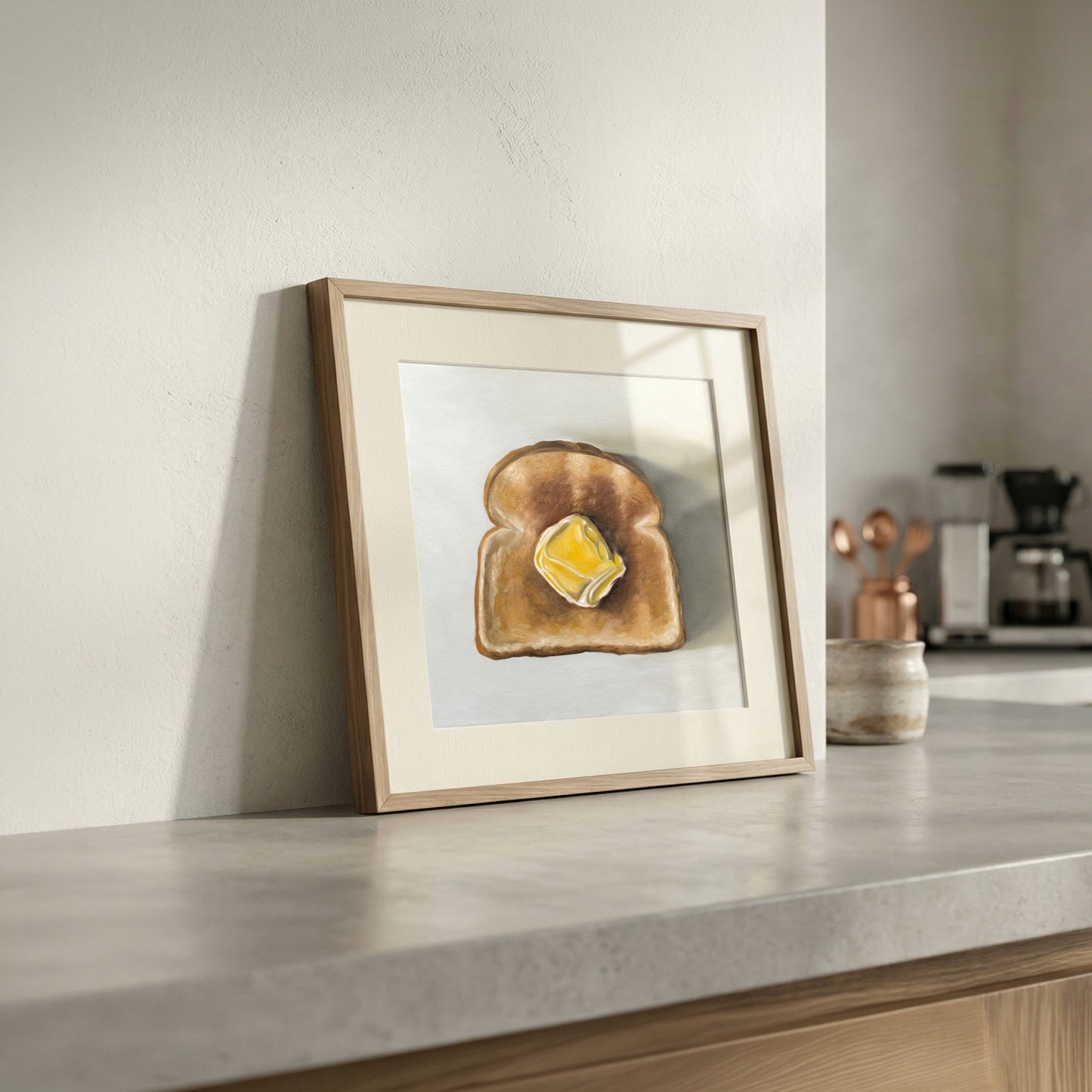 Framed fine art print of a golden brown toast slice with melting yellow butter, displayed on a kitchen counter.