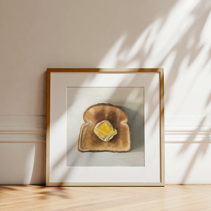 Buttered Toast fine art print in a light wood frame, leaning against a white wall with sun shadows.